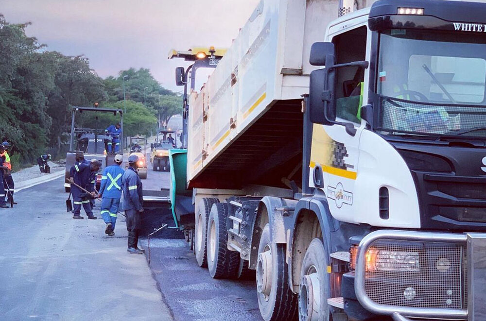 Tipper truck feeding an asphalt paver at dusk